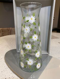 a glass vase with daisies painted on it sitting in front of a white box