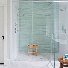 a bathroom with a walk in shower next to a wooden table and stool on the floor