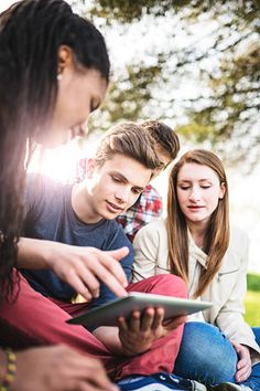 three young people sitting on the ground looking at something on an electronic device while one woman looks down