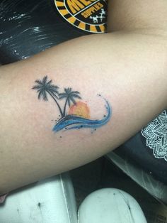 a woman's arm with a palm tree and wave tattoo on it