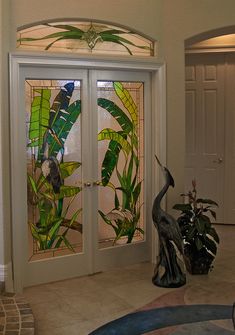 two birds are sitting on the floor in front of a glass door that is decorated with tropical plants