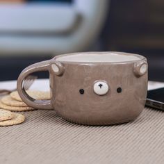 a coffee cup with a bear face on it next to crackers and a cell phone