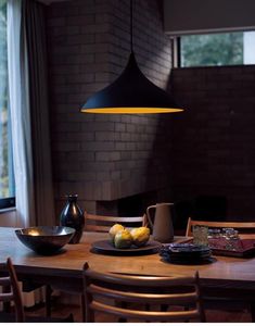 a wooden table topped with plates and bowls of fruit next to a lamp hanging from the ceiling