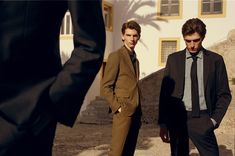 two men standing next to each other in front of a white building with palm trees