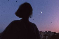 a person standing in front of a purple sky with birds flying over the city at night