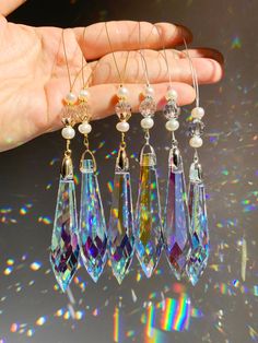 a hand is holding five different colored crystal drop earrings with pearls and beads hanging from them