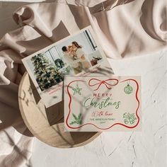 two christmas cards sitting on top of a wooden plate next to a white cloth covered wall