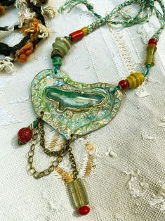 A pretty heart, rustic and naive style, in polymer inlaid with an agate, charms and Nepalese beads, green-red. Be unique! Each piece of jewelry only exists in one copy and you will be the only one to wear it. The plastron pendant: a heart, irregularly shaped, in textured, tinted and patinated ecru polymer (10.5 cm by 7 cm). I inlaid a green-white geode agate (7 cm by 2.5 cm) and I also decorated it with a bronze chain and charms: Tibetan red glass bead + green-white African trade bead and, on th Diy Jewellery Designs, Pretty Heart, African Trade Beads, Trade Beads, Red Bead, Red Silk, Green Bead, Red Glass, Jewelry Creation