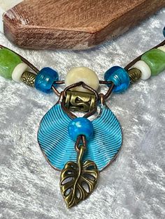 Colorful Turquoise Patina and Bronze charm woven on 1mm Bronze Leather cord with a Bronze Leaf charm and Blue Bone. Mated with bright blue Pony, Peridot color agate, white Bone and Bronze beads come together on two 1mm bronze leather cords with a decorative bronze "S" clasp for closing. Charm is 1" round and total length of necklace is 22". No lead or nickel used. Please use the Last On, First Off approach. Stones discolor with lotions, perfumes, hairspray, sweat, chlorine, even some soaps, and will break if dropped. Hippie Green Round Beads Jewelry, Bohemian Spacer Beads Necklace For Vacation, Hippie Green Round Beaded Jewelry, Nickel Free Multicolor Bohemian Beaded Necklaces, Artisan Necklace With Spacer Beads For Beach, Bohemian Multicolor Nickel-free Beaded Necklaces, Hippie Green Jewelry With Colorful Beads, Artisan Green Jewelry For Beach, Bohemian Multicolor Nickel-free Necklaces