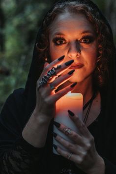 a woman with dark makeup holding a candle in her hands and looking at the camera