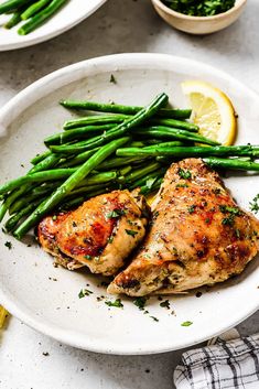 two white plates with chicken, asparagus and lemon wedges on the side