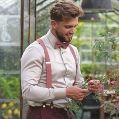 a man in a bow tie and suspenders is looking down at some pink flowers