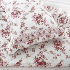 a white bed with pink flowers on it and two pillow cases next to each other