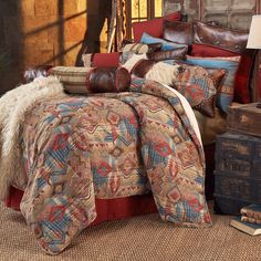 a bed covered in pillows and blankets next to an old trunk with luggage on it