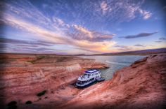 a boat that is floating in the water near some rocks and sand with a sunset behind it