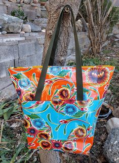 an orange and blue flowered bag hanging from a tree in front of some rocks