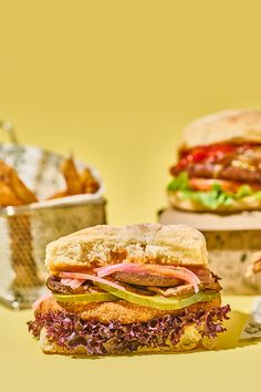 two sandwiches sitting next to each other on top of a table with french fries in front of them