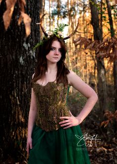 a woman wearing a green dress standing in front of a tree with horns on her head