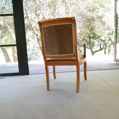 a wooden chair sitting on top of a white floor next to a glass door with trees in the background