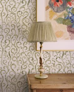 a lamp sitting on top of a wooden table next to a wallpapered wall