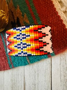 a colorful beaded bracelet sitting on top of a white wooden floor next to a ball of yarn