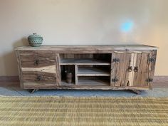 a wooden entertainment center with two doors and drawers on the bottom, in front of a beige wall