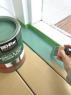 a person holding a paint brush and painting the outside of a window with green paint