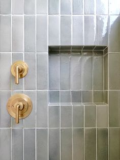 two gold faucets on the side of a tiled shower