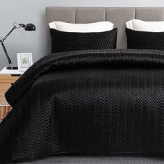 a bed with black comforter and pillows on top of it in a gray room