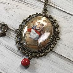 Here is a handmade necklace that was made using a rare mustard and red acrylic lovers cameo. The cameo is made in a fun French baroque style. It is made form an acrylic. It is set in a scalloped edge setting with a vintage red rhinestone dangle. The pendant hangs on an antique brass chain that closes with a lobster claw clasp.Size Pendant 2 7/8 by 1 7/8 inches Chain 25 inches Vintage Bronze Necklace For Valentine's Day, Vintage Bronze Necklaces For Valentine's Day, Antique Red Necklaces With Vintage Charm, Red Vintage Necklace With Charm, Red Cameo Necklace For Gift, Red Vintage Necklace With Cabochon, Vintage Red Cabochon Necklace, Vintage Red Oval Pendant Necklace, Red Cameo Jewelry Gift