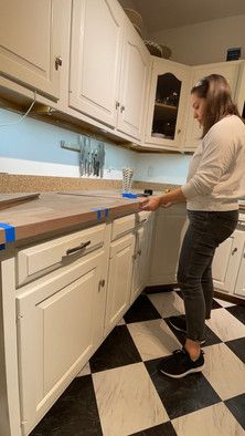 a woman standing in a kitchen next to a counter with blue tape on it and black and white checkered floor