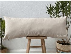 a white pillow sitting on top of a wooden stool next to a potted plant