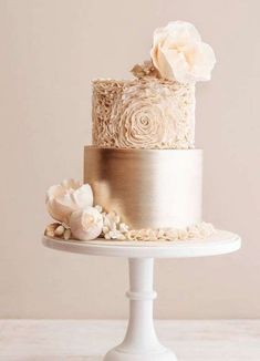 a three tiered cake with white flowers on the top and gold trimmings