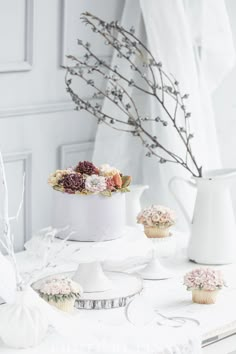 a white table topped with a cake and cupcakes next to a vase filled with flowers