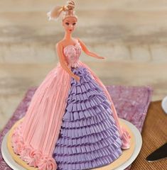 a barbie doll cake sitting on top of a plate next to a knife and fork