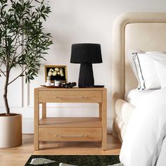 a bed room with a neatly made bed and a night stand next to a potted plant