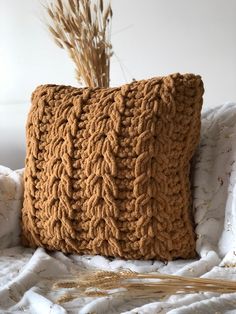 a crocheted pillow sitting on top of a bed next to a dried plant