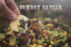 a hand holding a tortilla filled with black beans, corn and guacamole