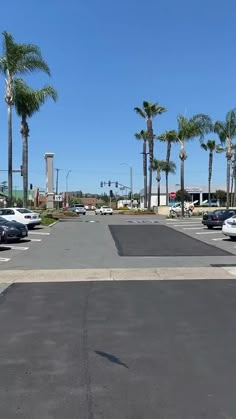 an empty parking lot with several cars parked in it and palm trees lining the street