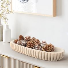 there are pine cones in the bowl on the counter next to vases and flowers