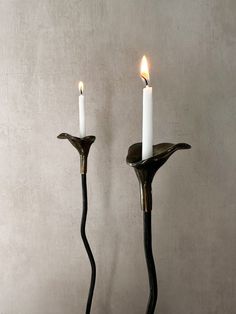 two candles are sitting next to each other on a table in front of a wall