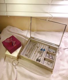 an open jewelry box sitting on top of a bed next to a pair of scissors