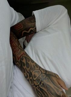 a man laying in bed with his arm covered by tattoos and holding a laptop computer