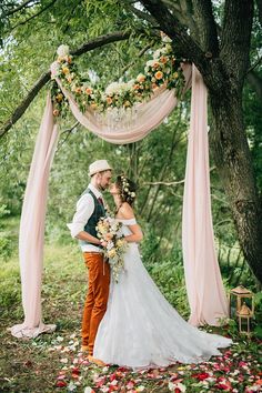 a bride and groom standing under an outdoor wedding ceremony arch with pink draping