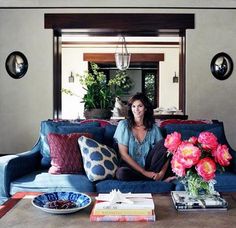 a woman sitting on top of a blue couch in front of a table with flowers