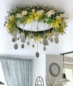 a clock and flowers hanging from the ceiling in a room with blue drapes on the windowsill