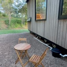 two chairs and a table in front of a small house with a gravel lot next to it