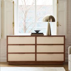 a white dresser sitting in front of a window next to a lamp on top of a rug