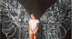 a woman standing in front of a wall with wings painted on it