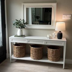 a white console table with three baskets on top and a mirror above it, in front of a window